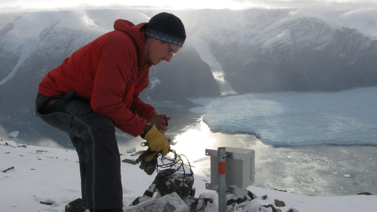 蒂姆·巴塞洛默斯(Tim Bartholomaus)倚在地震仪前，身后是冰川和山脉.